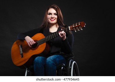 Real People, Disability And Handicap Concept. Teen Girl Handicapped Guitarist Sitting On Wheelchair Holds Guitar, Studio Shot On Dark