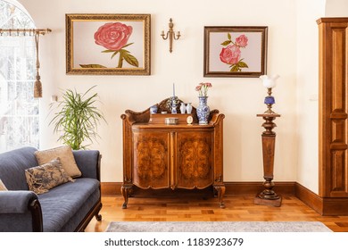 Real photo of an antique cabinet with porcelain decorations, paintings with roses and blue sofa in a living room interior