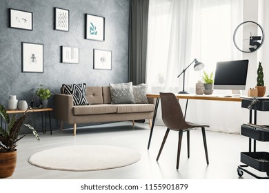 Real photo of a bright home office interior with a sofa, graphics, desk with a computer and lamp and modern clock - Powered by Shutterstock