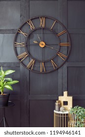 Real Photo With Close-up Of Big Clock Hanging On Black Wall In Dark Living Room Interior With Gold Accessories And Fresh Plants