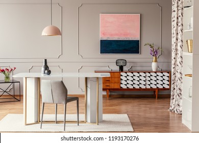 Real photo of a dining room interior with a table, pink painting and vintage cabinet