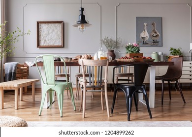 Real photo of an eclectic dining room interior with various chairs at the table, lamp and painting with ducks