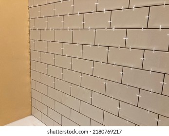 A real photo of laying tiles on the wall. Stained white ceramic tile and a layer of tile glue on the wall. Plastic tile spacer or tile cross between tiles. 