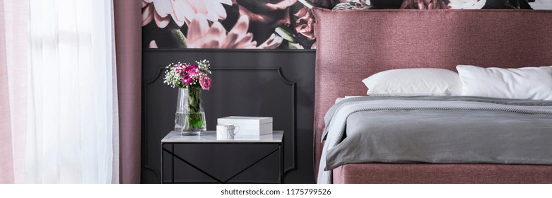 Real Photo Of Marble Bedside Table With Tea Cup, Box And Fresh Flowers Standing By The Bed In Dark Grey Room Interior With Window With Drapes