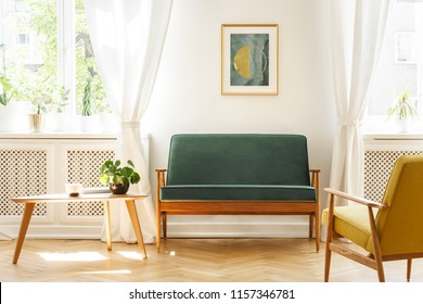 Real photo of a mid-century living room interior with a sofa, coffee table, windows and painting