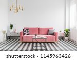 Real photo of a modern living room interior with a checkered floor, pink couch, coffee table and empty, white wall. Place your graphic here