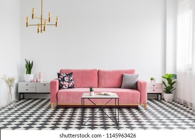 Real photo of a modern living room interior with a checkered floor, pink couch, coffee table and empty, white wall. Place your graphic here