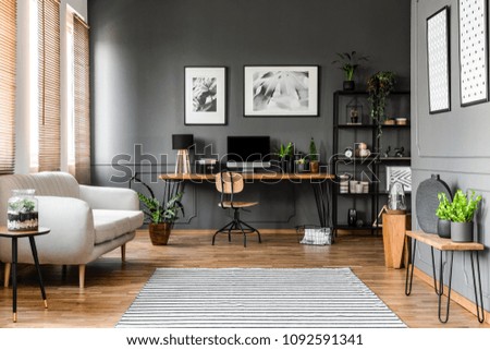 Real photo of open space apartment interior with beige sofa next to the window and desktop computer o a wooden desk