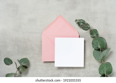 Real Photo. Pink Envelope Square Invitation Card Mockup With A Eucalyptus Branch. Top View With Copy Space, Light Gray Concrete Background. Template For Branding And Advertising