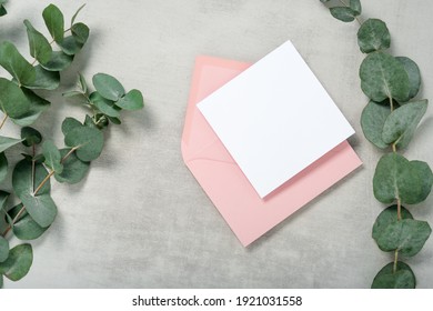 Real Photo. Pink Envelope Square Invitation Card Mockup With A Eucalyptus Branch. Top View With Copy Space, Light Gray Concrete Background. Template For Branding And Advertising