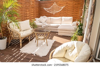 Real photo of relaxing boho zone in home. Wooden floor on terrace with comfy furniture and green plants. Decoration concept. Sunny summer day.