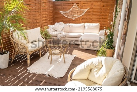 Real photo of relaxing boho zone in home. Wooden floor on terrace with comfy furniture and green plants. Decoration concept. Sunny summer day.