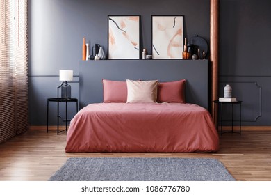 Real Photo Of A Simple Bedroom Interior With Dirty Pink Bedding On The Bed Standing Against Dark Gray Wall With Molding, Between Two, Metal Bedside Tables