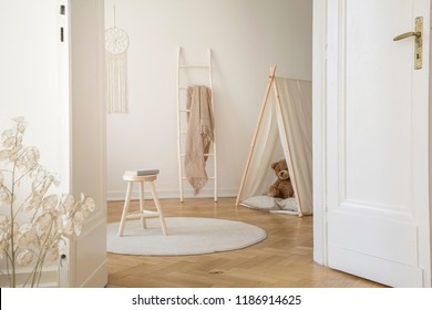 Real Photo Through The Door Of Kid Room Interior With Blanket On Ladder, Stool With Book, Play Tent With Teddy Bear And Herringbone Parquet