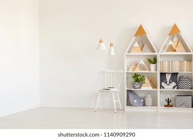 Real photo of white kid room interior with two lamps, mountain shape rack with books and decor and empty place for your bed
