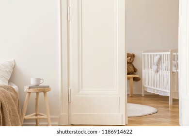 Real Photo Of Wooden Stool With Book And Tea Mug Standing Next To White Door To Kid Room Interior With Crib And Herringbone Parquet