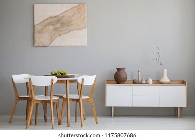 Real Photo Of Wooden Table And Four Chairs Standing In Light Grey Dining Room Interior With Modern Art Poster And Cupboard With Decor