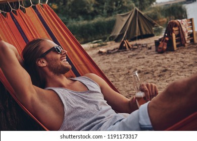 Real relaxation. Handsome young man keeping hand behind head and smiling while lying in hammock - Powered by Shutterstock