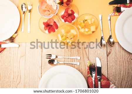 real set breakfast table with small glass bowls full of fruits and fish, yellow tablecloth, silver cutlery, white plates on wooden table