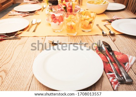 real set breakfast table with small glass bowls full of fruits and fish, yellow tablecloth, silver cutlery, white plates on wooden table