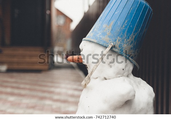 Real snowman from snow with bucket hat on the\
snowy street in backyard