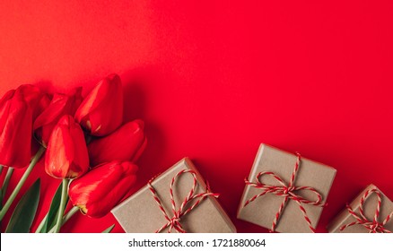 Real spring red tulips and gift box on a red background. Spring flowers for Mother's Day. Top view. Flat lay