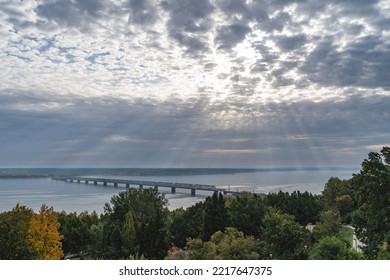 Real sun rays through the clouds in the sky the bridge across the Volga river in Ulyanovsk, built under the tsar in Russia. Operating iron bridge. Connects two shores of one city - Shutterstock ID 2217647375