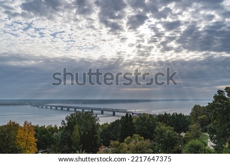 Real sun rays through the clouds in the sky the bridge across the Volga river in Ulyanovsk, built under the tsar in Russia. Operating iron bridge. Connects two shores of one city