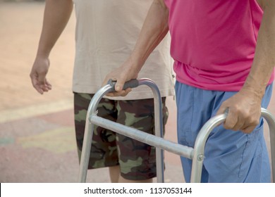 Real View Of Senior Man 80 Year Who Has Paralysis Or Palsy Or Disability With Son Or Asian Freelance Nurse To Take Care. Old Man Holding A Walker Aid Support. Concept Freelance Nurse Helpful.