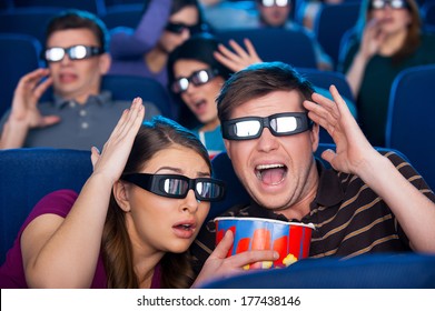 So realistic movie! Shocked young people in three-dimensional glasses gesturing while watching movie at the cinema together