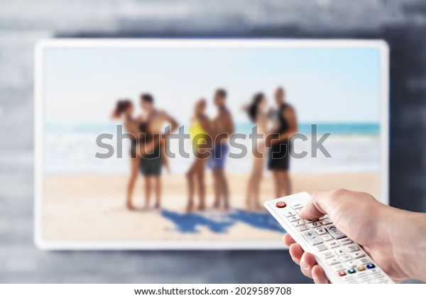 Reality tv show stream on television.\
Watching series on VOD streaming service. Couples at the beach or\
island dating, looking for love. Person using remote control.\
Contest or celebrity\
entertainment