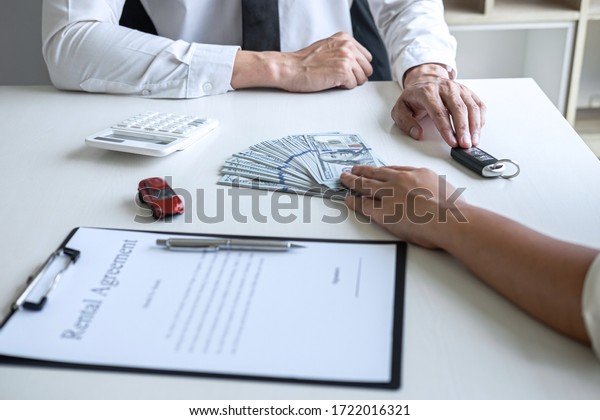 Realtor agent\
manager holding key of new car giving to woman client after signing\
rental contract form and sending dollar us banknotes, renting\
considering vehicle car\
insurance.