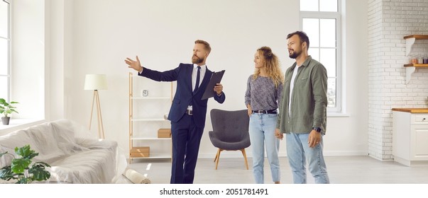 Realtor giving future tenants or first time buyers tour about modern apartment. Boyfriend and girlfriend or husband and wife planning to buy new home and meeting with real estate agent in new house - Shutterstock ID 2051781491