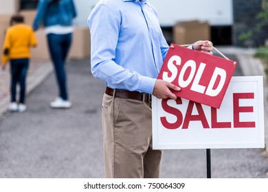 Realtor Hanging Sold Sign In Front Of People Moving Into New House