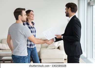 Realtor or landlord handshaking couple buyers tenants make real estate deal holding rental agreement or sale purchase contract, agent and clients shake hands welcoming renters in new home apartment - Shutterstock ID 1302585028