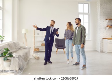 Realtor or real estate agent giving potential buyers or tenants tour about big house. Boyfriend and girlfriend or husband and wife who consider buying property looking at new modern spacious home