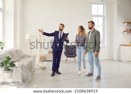 Realtor or real estate agent giving potential buyers or tenants tour about big house. Boyfriend and girlfriend or husband and wife who consider buying property looking at new modern spacious home
