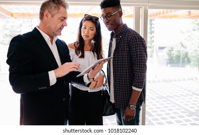 Realtor showing terms of contract on tablet to interracial couple. Real estate agent sharing property details with clients. - Shutterstock ID 1018102240