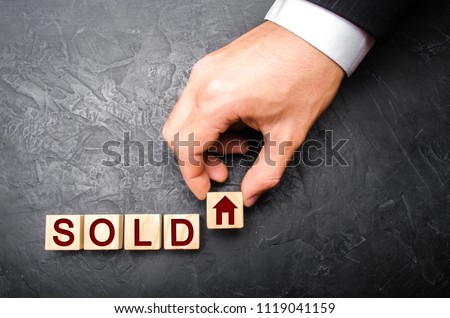 realtor's hand puts a cube with a picture of the house to the word sold. Concept of selling a house, apartment, real estate. market of immobility. Trade of property. Affordable housing. Hand in suit.