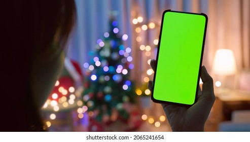 rear of asian woman watch green screen smartphone with christmas decoration and tree at home - Powered by Shutterstock