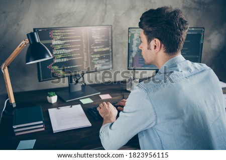 Rear back behind view portrait of his he nice attractive focused geek guy typing css analyzing cyberspace security building at modern industrial interior style concrete wall work place station