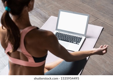 Rear back over shoulder view at fit sporty healthy calm woman sit on mat in lotus pose watching online yoga class meditate do breathing exercises on laptop computer blank white mock up screen concept - Powered by Shutterstock