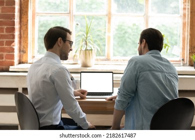 Rear Back Two Colleagues Teammates Discuss Strategy, Work On Collaborative On-line Project Sit At Desk With Laptop, White Mock Up On Device Screen. Website, Connection, Workflow, Partnership Concept