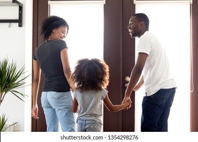 Rear back view afro black parents hold hands little preschool adorable daughter family go for a walk standing in doorway hallway of modern new house. Free time communication leisure activities concept