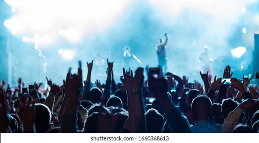 Rear Back View Of Audience Crowd People Fans Raising Hands Enjoying Live Music Festival Concert Event Concept Shooting On Phones Rock Band Silhouettes Performance Sing On Night Club Outdoor Stage.