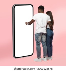 Rear Back View Of Black Couple Using Big Smartphone With Blank White Screen Touching Huge Display Panel With Finger, Guy Higging Lady Standing On Pink Background, Mock Up. Full Body Length - Shutterstock ID 2109126578