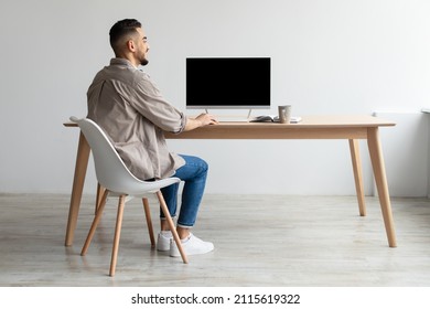 Rear Back View Of Happy Smiling Arab Man Looking At Pc Computer With Blank Black Screen For Mock Up Template Sitting At Desk At Home Office, Free Copy Space. People, Technology, Remote Work Concept - Shutterstock ID 2115619322