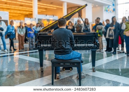 Rear back view of a man playing the piano in a public place and blurred people watching him