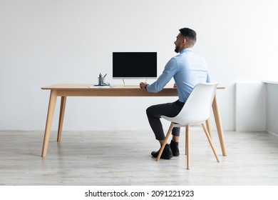 Rear Back View Portrait Of Middle Eastern Businessman Looking At Blank Empty Computer Monitor Sitting At Desk At Workplace, Watching Webinar Or Having Online Web Video Call, Free Copy Space Banner