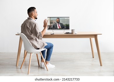 Rear Back View Of Smiling Young Arab Business Man Making Video Call With Black Colleague Using Laptop At Office, Having Web Conference Waving Hand At Computer Web Camera And Talking. Remote Work